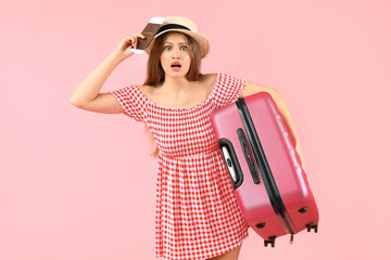 Shocked female tourist with luggage on color background