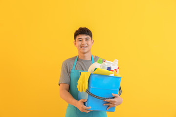 Asian man with cleaning supplies on color background