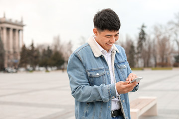 Young Asian man with mobile phone outdoors