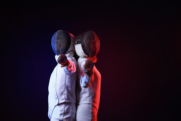 Toned photo of young fencers on dark background