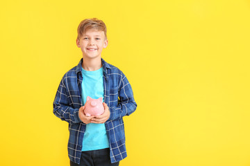 Cute boy with piggy bank on color background