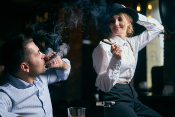 The man-gangster and the beautiful senior woman smoking cigar in a bar
