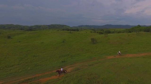 Two riders galop their horses in a red dirt road in a venezuelan plain, slow motion