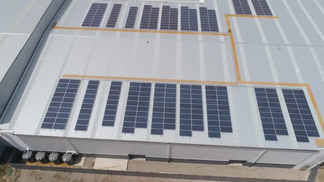 Aerial close up rising to reveal solar panel package installation on warehouse rooftop