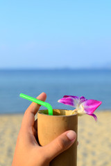 Welcome drink with bamboo glass and decorate with purple orchid on sand, sea and blue sky background.