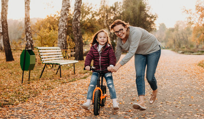 A cheerful young mother who is teaching her small and smiling daughter to ride the bike in a sunny autumn evening