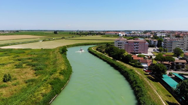 Livenza River canal with a boat after exiting the Adriatic through Porto Santa Margherita, Caorle Italy, Aerial drone flyover shot