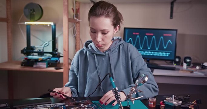 Woman electronics engineer is soldering an electric board in her workshop. Girl student are studying electronics and soldering in classroom.