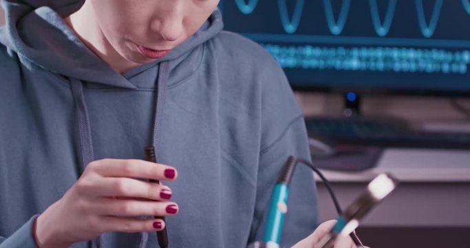 Woman electronics engineer is soldering an electric board in her workshop. Girl student are studying electronics and soldering in classroom.