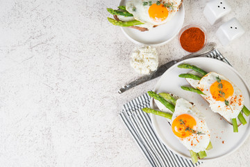 Crispy toast with cream cheese cream, fried egg and asparagus in a plate on a white background.