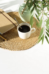 Lifestyle composition with coffee cup , notebook and eucalyptus leaves with shadows on white table ...
