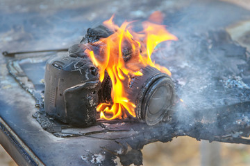 on a charred table is a burning digital SLR camera