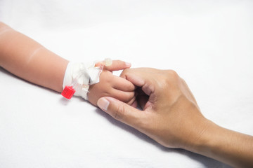 Mother holding baby hand give saline solution in bed fever patients in hospital.