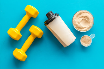 Sport diet. Protein shake near dumbbells on blue background top-down flat lay copy space