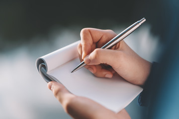 Woman hand holding notebook and pen at outdoor park.