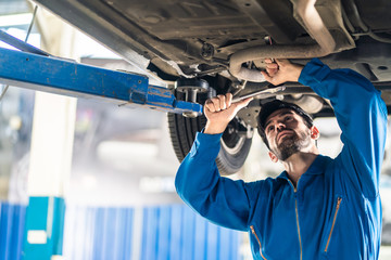Vehicle service maintenance handsome mens checking under car condition on lifter hoist in garage. Automotive mechanic man use tool to tighten and replace damaged or broken part. Repair service concept