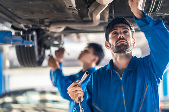 Vehicle service maintenance handsome mens checking under car condition on lifter in garage. Automotive mechanic man use tool to tighten and replace damaged or broken part. Car repair service concept.