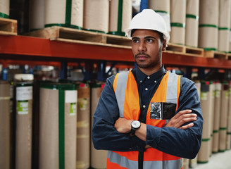 Portrait of a young serious african american man with folded hands and white hard hat standing in...