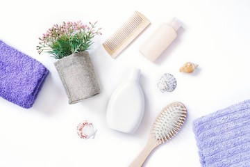 Flat lay photo purple towels, wooden hair brushes, moisturizing shampoo, nourishing balm, flowers and seashells on white background