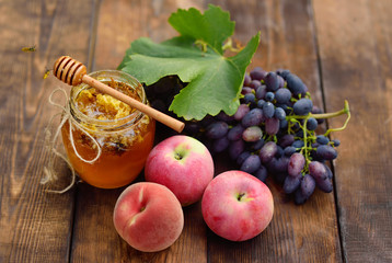 The wasps fly around the jar with honey, grapes and apples on a wooden background