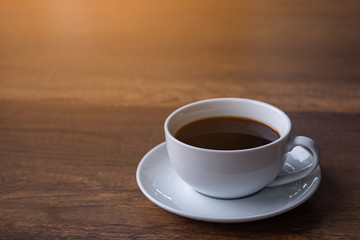 A white cup of coffee on wooden table with sunlight. Space for text. Relax in the morning. Relaxation concept