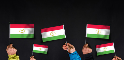 Fototapeta na wymiar Hands holds flags of Tajikistan on dark background