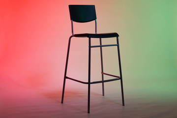 A tall chair stands in a photo studio on a white paper background lit in red-green tones