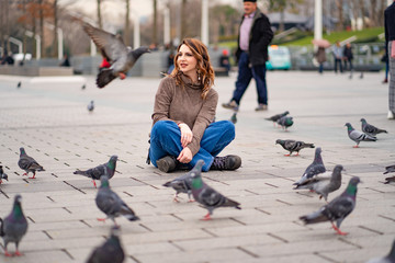 Obraz premium The girl sits on the square and around the pigeons