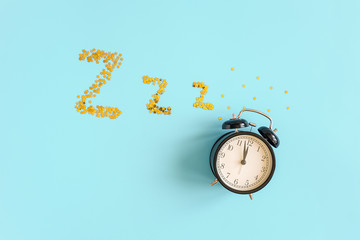 Black alarm clock and gold stars confetti in form of dream symbols Z Z Z on blue background. Top view Copy space. Concept Insomnia, sleep problems or sweet dreams and good night.