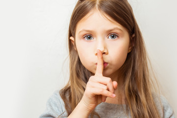 Naklejka premium Portrait of beautiful child girl with finger on lips, isolated over white background