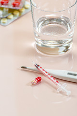 Pill, syringe and thermometer on a beige pastel background.