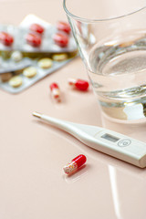 Antibiotic tablet, a glass of water and a thermometer on a beige pastel background.