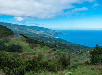 Subtropical landscape with green hills, tree, houses, winding alphalt road and sea horizon. Blue sky white clouds background, La Palma, Canary Islands, Spain
