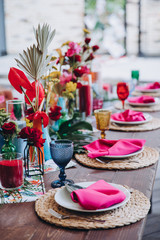 Banquet tables decorated in tropical style decor, dishes on the tables with pink napkins, glasses,...