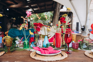 Banquet tables decorated in tropical style decor, dishes on the tables with pink napkins, glasses, candles, colorful flowers