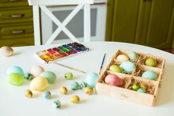 Colored Easter eggs with paints and brushes on a white table