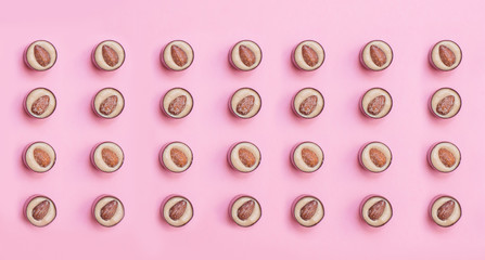 Round pattern chocolates with pistachio cream and salted almonds on pink background. Flat lay