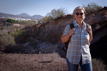 Attractive senior female with gray hair walking in the footpath with a backpack.  Excursion in a mountain site