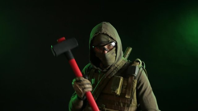 soldier-saboteur in military clothing with a weapon on a dark background in the hands of a sledgehammer