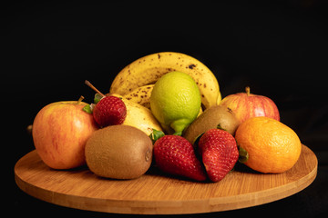 Fruta variada sobre tabla de madera en fondo negro