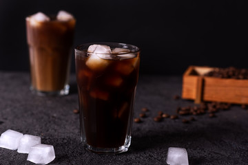 Iced coffee in a tall glass with cream poured over. Wood background. Low key.