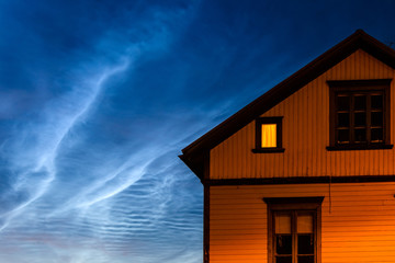 Close-up of cottage with one window lit against dramatic night sky, Sweden.