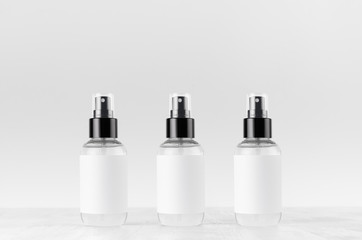 Three transparent spray bottles for cosmetics product with white blank label on white wood board, mock up for branding, advertising, design.