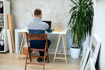 Back view of an Attractive freelance male sitting in modern office and typing on notebook.	