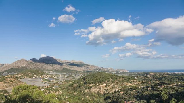 Clouds appear over mountainous terrain with the mediterranean sea in the background.