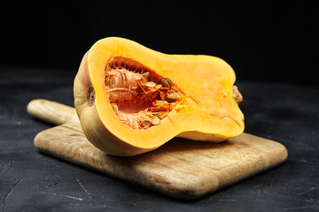 Butternut squash half with seeds on wooden cutting board on black background. Pumpkin seeds. Cooking winter squash