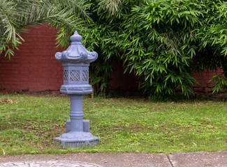 Front view of a lamp post with brick wall in the background covered by bamboo leaves. Zen concept