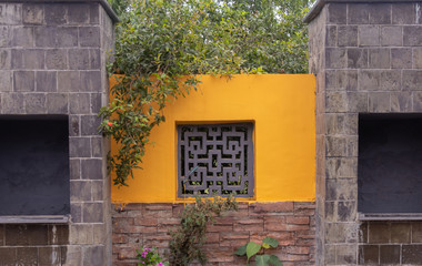 Front view of a yellow wall made of stones and bricks with tree branches covering it. Buddhism...