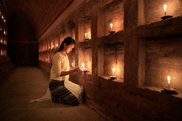 Obraz na płótnie Canvas Young Burmese girl prays by candlelight in Bagan, Myanmar