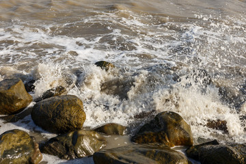 sea waves break on large stones on the shore forming sea foam